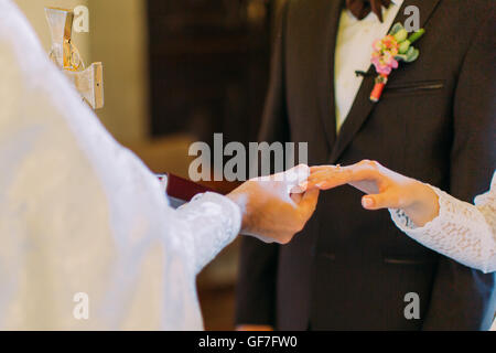 Priester setzt den Ring am Finger der Braut während der Trauung Stockfoto