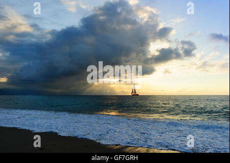 Segelboot-Silhouette ist ein Burst Sonnenstrahlen durch die Wolken schießen wie ein Segelboot entlang des Wassers in Richtung des Lichts bewegt. Stockfoto