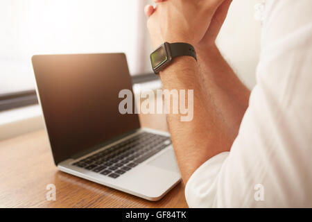 Nahaufnahme der Mann sitzt an seinem Schreibtisch mit Laptop, er trägt eine Smartwatch. Stockfoto