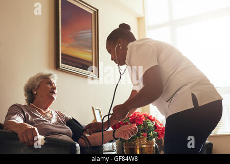 Ältere Patienten mit ihrer Krankenschwester im Wohnzimmer auf dem Sofa sitzen. Ärztin, die Messung des Blutdrucks von Old Lady. Stockfoto