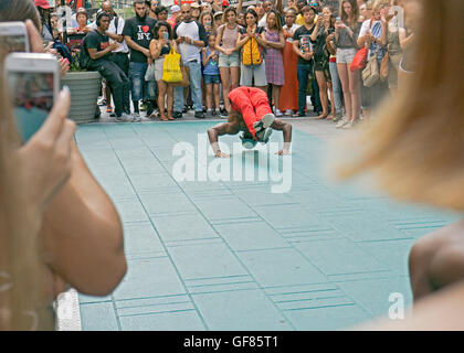 Eine akrobatische sportlich Straße Straßenmusiker auf dem Times Square macht einen Handstand für eine große Menge von Touristen Stockfoto