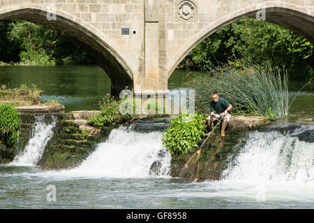 Fischer auf Bathampton Wehr mit Rute und Net. Amateur Angler schöpft Fische ins Netz am Wasserfall im Fluß Avon Stockfoto