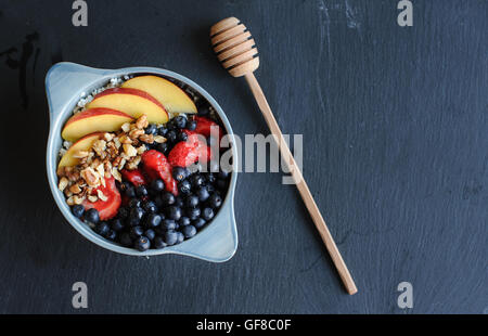 Gesundes Frühstück in blau Schüssel mit Obst Toppings und Honig-Stick. Frühstück mit Quark, Honig, Pfirsich, Walnüsse Stockfoto