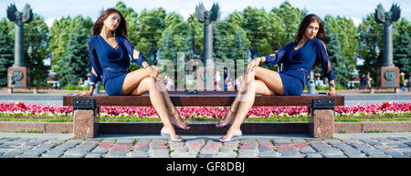 Schöne junge Frau sitzt auf einer Bank in einem Sommerpark Stockfoto