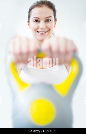 EIGENTUM FREIGEGEBEN. -MODELL VERÖFFENTLICHT. Lächelnde junge Frau mit Kettlebell im Fitness-Studio, Porträt. Stockfoto