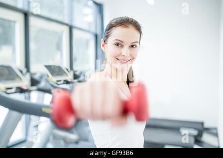 EIGENTUM FREIGEGEBEN. -MODELL VERÖFFENTLICHT. Lächelnde junge Frau mit Hantel im Fitness-Studio, Porträt. Stockfoto