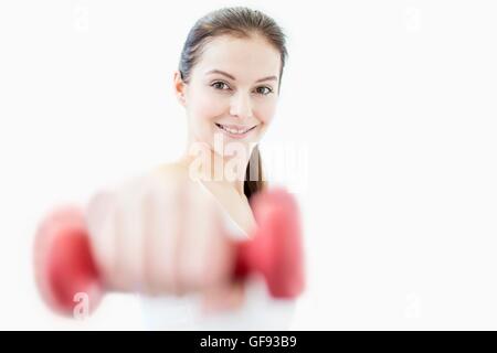 EIGENTUM FREIGEGEBEN. -MODELL VERÖFFENTLICHT. Lächelnde junge Frau mit Hantel im Fitness-Studio, Porträt. Stockfoto