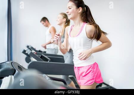 EIGENTUM FREIGEGEBEN. -MODELL VERÖFFENTLICHT. Junger Mann und Frauen, die auf Fitnessgeräte im Fitness-Studio. Stockfoto