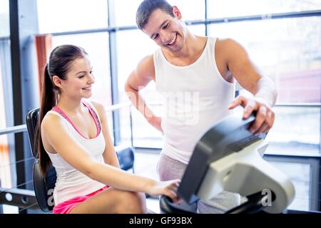 EIGENTUM FREIGEGEBEN. -MODELL VERÖFFENTLICHT. Mann anweist Frau zur Ausübung Maschine Verwendung in Fitness-Studio, lächelnd. Stockfoto
