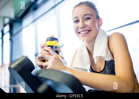 EIGENTUM FREIGEGEBEN. -MODELL VERÖFFENTLICHT. Junge Frau mit Flasche Wasser beim Training im Fitness-Studio, Lächeln, Porträt. Stockfoto
