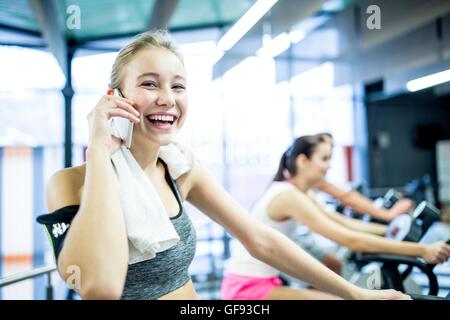 EIGENTUM FREIGEGEBEN. -MODELL VERÖFFENTLICHT. Porträt der jungen Frau telefonieren mit Handy während der Arbeit im Fitness-Studio, lächelnd. Stockfoto
