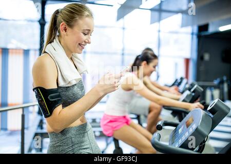 EIGENTUM FREIGEGEBEN. -MODELL VERÖFFENTLICHT. Junge Frau SMS auf Handy während der Arbeit im Fitness-Studio, lächelnd. Stockfoto