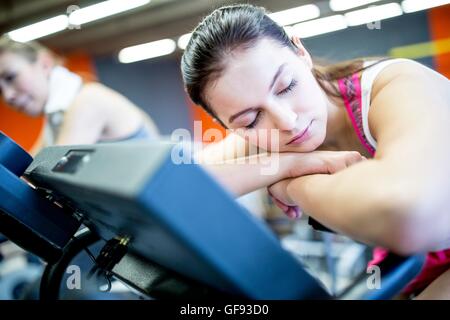 EIGENTUM FREIGEGEBEN. -MODELL VERÖFFENTLICHT. Nahaufnahme der jungen Frau ruht auf Heimtrainer mit geschlossenen Augen in Fitness-Studio. Stockfoto