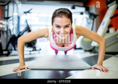 EIGENTUM FREIGEGEBEN. -MODELL VERÖFFENTLICHT. Porträt der jungen Frau Liegestütz im Fitness-Studio zu tun. Stockfoto