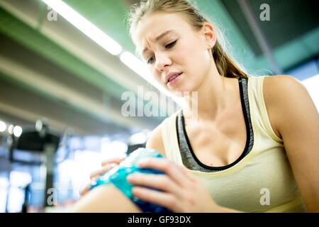 EIGENTUM FREIGEGEBEN. -MODELL VERÖFFENTLICHT. Junge Frau mit Eisbeutel auf verletzte Knie im Fitness-Studio. Stockfoto