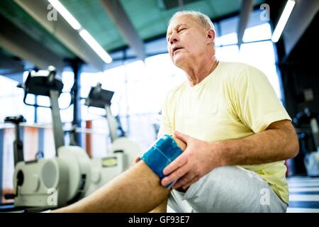 EIGENTUM FREIGEGEBEN. -MODELL VERÖFFENTLICHT. Senior woman holding Eisbeutel auf verletzte Knie im Fitness-Studio. Stockfoto