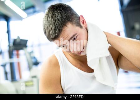 EIGENTUM FREIGEGEBEN. -MODELL VERÖFFENTLICHT. Junger Mann wischte sich sein Schweiß mit Handtuch nach dem Training im Fitness-Studio. Stockfoto
