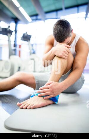 EIGENTUM FREIGEGEBEN. -MODELL VERÖFFENTLICHT. Junger Mann Betrieb Eisbeutel auf verletzten Knöchel im Fitness-Studio. Stockfoto