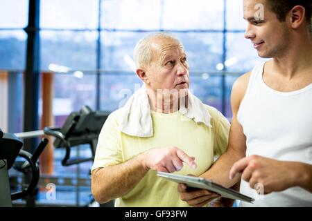 EIGENTUM FREIGEGEBEN. -MODELL VERÖFFENTLICHT. Junge Gym Trainer halten digital-Tablette und im Gespräch mit älteren Mann im Fitness-Studio. Stockfoto