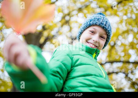 -MODELL VERÖFFENTLICHT. Lächelnde junge Wollmütze und Jacke hält Blatt, Porträt, Nahaufnahme. Stockfoto