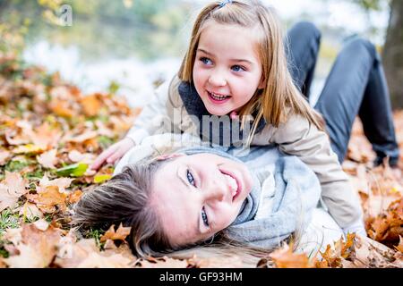 -MODELL VERÖFFENTLICHT. Mutter und Tochter auf getrocknete Blätter im Herbst liegen und lächelnd. Stockfoto