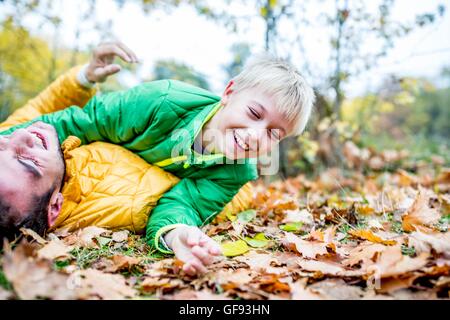 -MODELL VERÖFFENTLICHT. Vater und Sohn auf getrocknete Blätter im Herbst liegen und lachen. Stockfoto