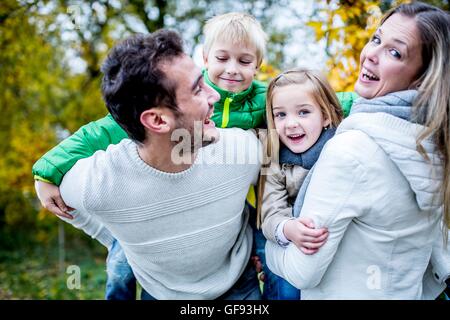 -MODELL VERÖFFENTLICHT. Eltern tragen ihre Kinder im Herbst, lachen. Stockfoto