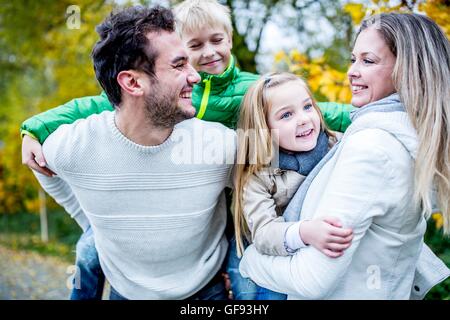 -MODELL VERÖFFENTLICHT. Eltern tragen ihre Kinder im Herbst, lachen. Stockfoto