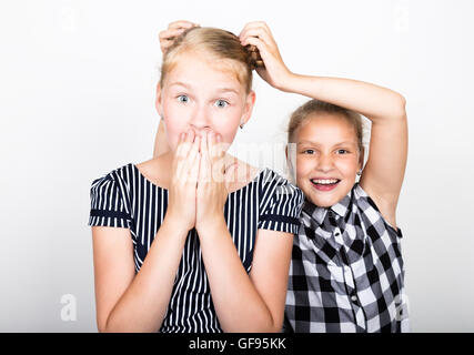 Zwei süße kleine Freundin mit dem Ausdruck ihrer verschiedene Emotionen. Lustige Kinder. Beste Freundinnen verwöhnen und posiert Stockfoto