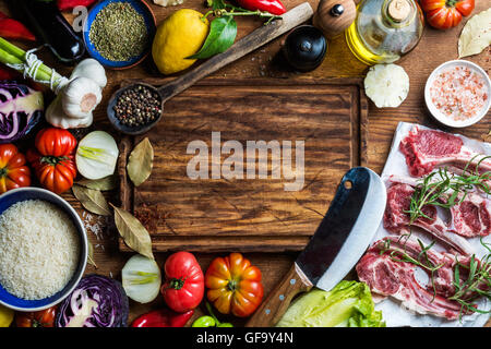 Zutaten für gesundes Fleisch Abendessen kochen. Roh, ungekocht Lammkoteletts mit Gemüse, Reis, Kräuter und Gewürze über rustikalen hölzernen Hintergrund, dunkel, Schneidebrett in Mitte Stockfoto