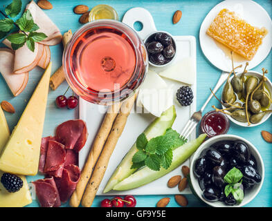 Sommerwein snack Set. Glas Rose, Fleisch, Käse, Oliven, Honig, Brot-Sticks, Nüssen, Kapern und Beeren mit keramischen Tafel im Zentrum, blauen hölzernen Hintergrund Stockfoto