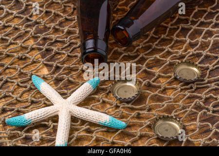 Leere Bierflaschen auf einem verwitterten Tisch gedeckt durch ein Fischernetz an der Strand-Seestern im Hintergrund Stockfoto