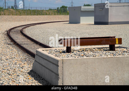 Ende der Schiene in einem Industriegebiet am Hintergrund der kiesigen Ufer und Strommasten Stockfoto