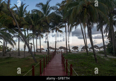 Holzweg mit Geländer, die einen schönen Strand mit Palmen, Sonnenschirme und Liegestühle erreicht Stockfoto