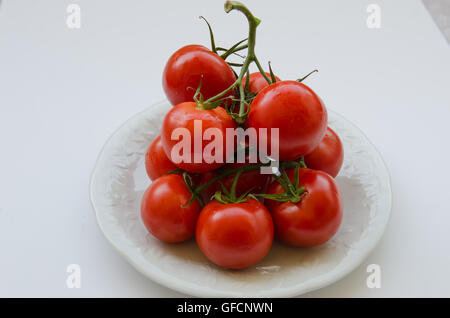 Stapel von rote Tomaten mit Stielen befestigt auf weißen Teller isoliert auf weißem Hintergrund Stockfoto