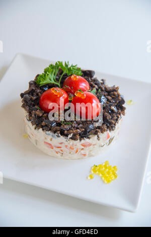 Russischer Salat mit Cherry-Tomaten, schwarzen Oliven, Petersilie und Perlen von Olivenöl. Stockfoto