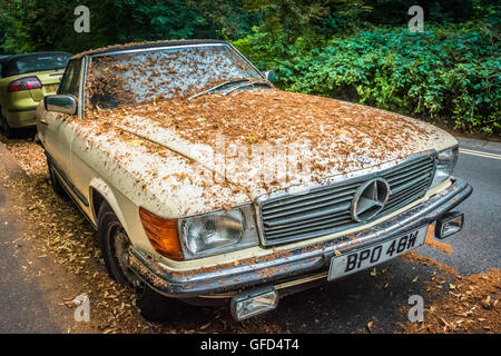 Ein verlassene Mercedes bedeckt in den Blättern in einer ruhigen Straße von London, UK Stockfoto