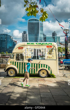 Ein Junge spielt vor einem Eiswagen neben London Bridge City Pier auf der Themse in London, UK Stockfoto