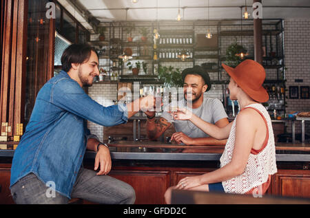 Drei junge Leute im Restaurant sitzen und mit einem Toast. Gruppe von Freunden in einem Café einen Drink und toasten.