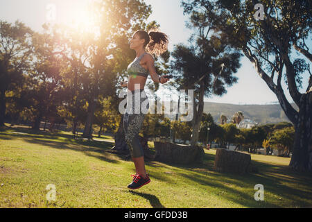 Seitenansicht der sportliche Frau, die in einem Park an einem sonnigen Morgen überspringen. Fit und athletisch weiblich Training mit einem Springseil auf die gras Stockfoto