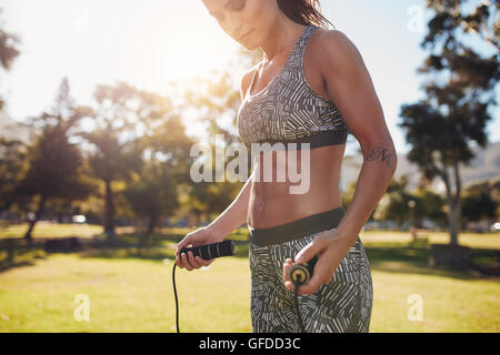 Außenaufnahme einer jungen Sportlerin, die draußen im Park ausspringt. Fitness-Frau, die an einem sonnigen Tag mit Sprungseil trainiert. Stockfoto