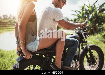 Schuss des Jünglings Fahrt auf einem Motorrad mit Freundin auf Landstraße beschnitten. Mann und Frau auf einem Motorrad fahren. Paar o Stockfoto