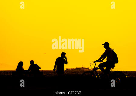 Silhouette Menschen in Izmir Türkei. Fahrrad fahren Mann, ein Telefon aufrufenden Mann und zwei Leute sitzen auf einer Bank in der Nähe der Küste ich Stockfoto