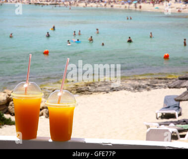 Zwei frisch gepressten Orangensaft in einen Plastikbecher mit einem Strohhalm auf Meer Hintergrund Stockfoto