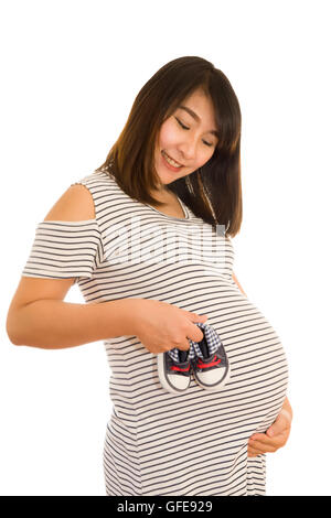 Kleine Schuhe für das ungeborene Kind in den Bauch der schwangeren Frau isoliert auf weiss Stockfoto