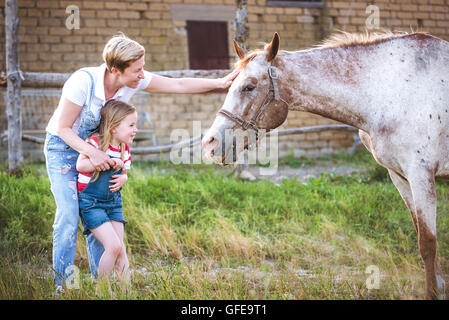 Mutter und Tochter, die Fütterung eines Pferdes eines Apfels im Gestüt. Stockfoto