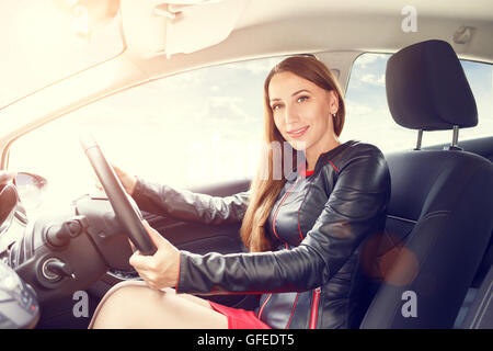 Junge schöne Frau-Lenkrad, ein Auto zu fahren. Zuversichtlich lächelnden Dame im roten Kleid, ein Auto zu fahren Stockfoto