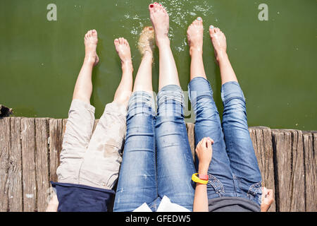 Mutter und ihre Kinder haben Spaß am Pier spritzt ihre Beine ins Wasser des Teiches. Glückliche Sommer Urlaub Hintergrund Stockfoto