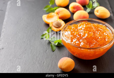 Marillenmarmelade in eine Glasschüssel, frischen Aprikosen auf schwarzem Stein Stockfoto