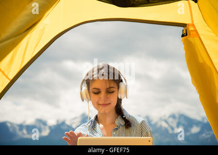 Mädchen im Zelt mit Kopfhörern Musik hören und mit Blick auf Tablet Stockfoto